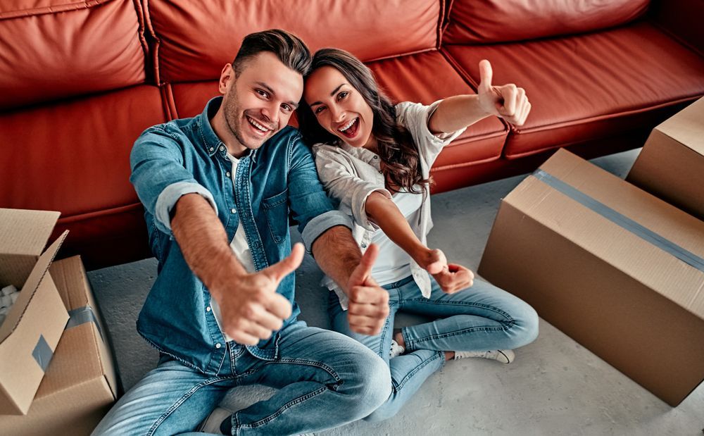 A man and a woman are sitting on the floor giving a thumbs up for the best movers in Virginia.