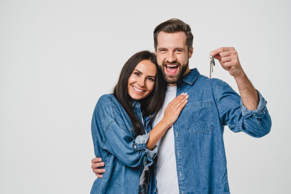 A man and a woman are standing next to each other holding keys to their new home after hiring moving company.