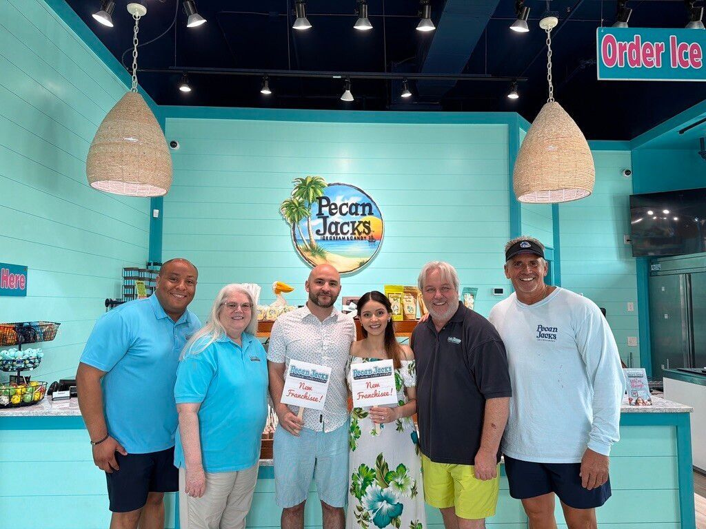Group of people posing outside a restaurant, smiling and raising their arms in front of the entrance.