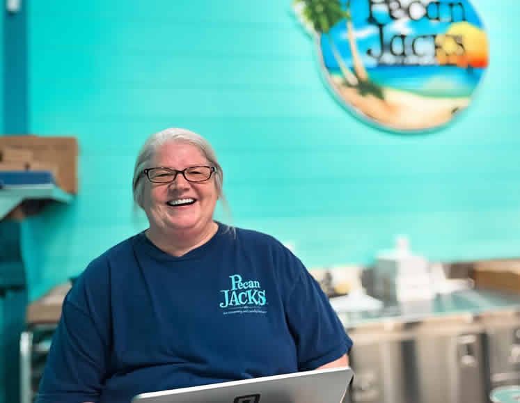 A woman in a blue shirt is smiling while holding a laptop.