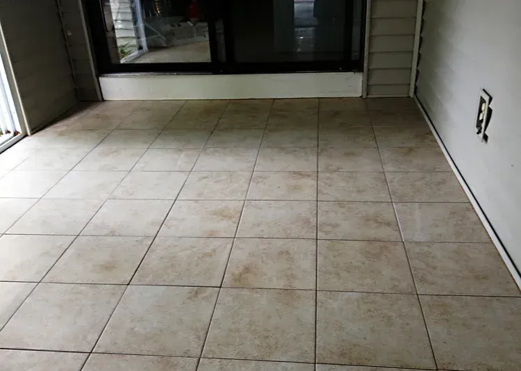 Tan tiled floor inside a room, with a dark window and a blank outlet visible.