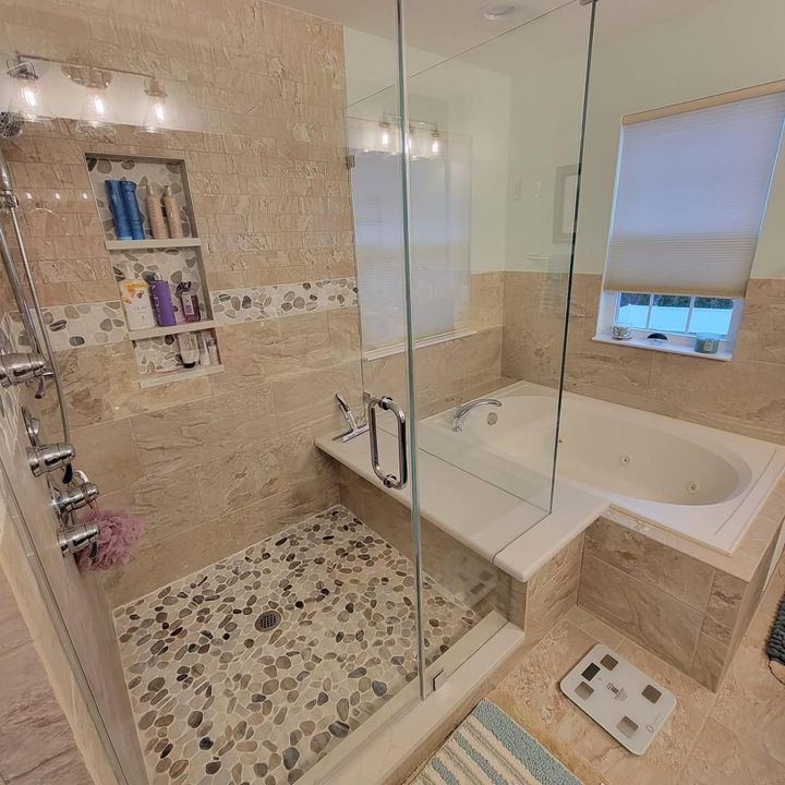 Bathroom with a glass shower door, pebble floor, built-in tub, and stone walls.