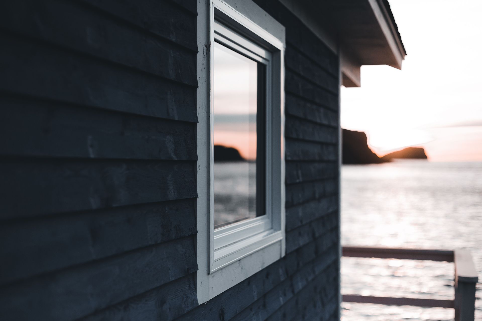 Dark blue house wall with a window overlooking a calm ocean at sunset