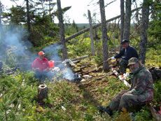 A group of men are sitting around a campfire in the woods.