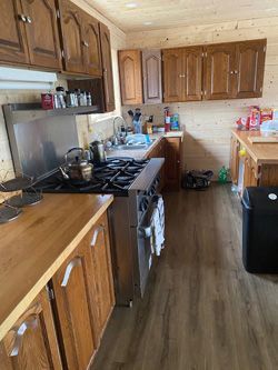 A kitchen with wooden cabinets , a stove , a sink and a trash can.