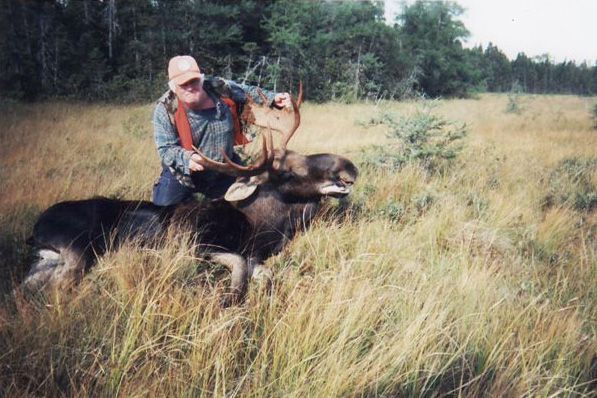 A man is standing next to a moose in a field.