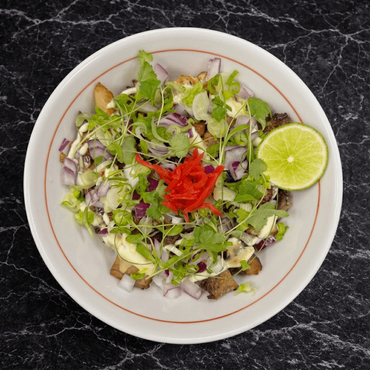 Salad with greens, red onion, and chili garnish on a white plate, with a lime wedge on the side