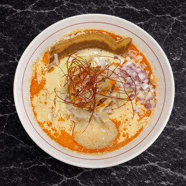 A bowl of ramen with pork belly, corn, menma, green onions, and a soft-boiled egg in a creamy, broth-based soup.