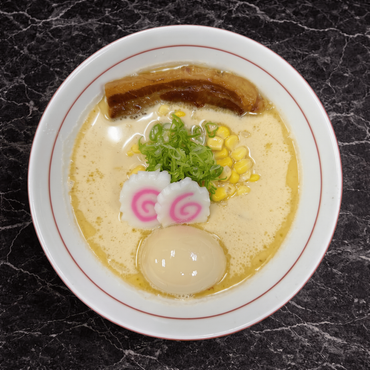 A bowl of ramen with a creamy broth, topped with bamboo shoots, two narutomaki slices, a soft-boiled egg, and green onions.