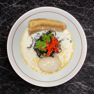 A bowl of ramen with pork belly slices, a soft-boiled egg, black fungus, pickled ginger, and green onions in broth.
