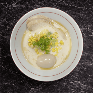 A bowl of ramen topped with grilled chicken, a soft-boiled egg, corn, wood ear mushrooms, and scallions in a creamy broth.