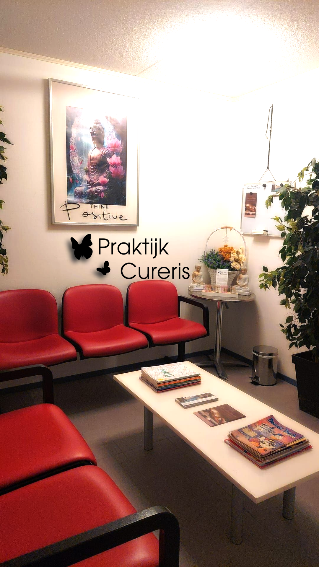 Wachtkamer met rode stoelen, tijdschriften op een witte tafel en kunst aan de muur.