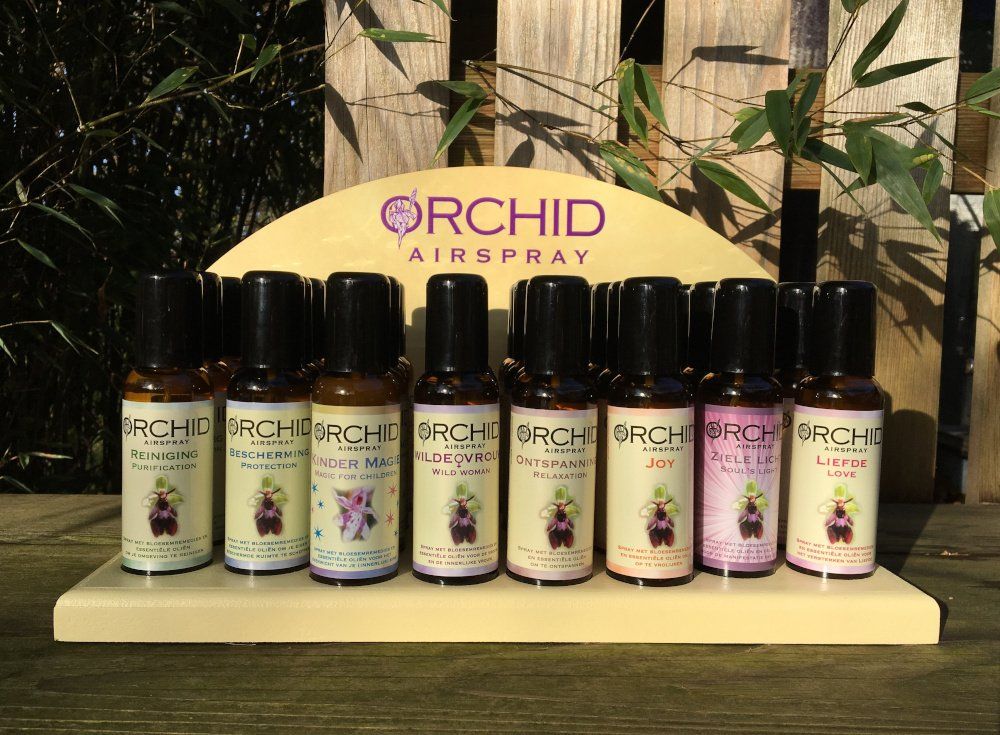 Presentatie van Orchid Airspray-flessen in een winkel. De flessen hebben verschillende kleuren en staan ​​tegen een gebogen schapachtergrond.