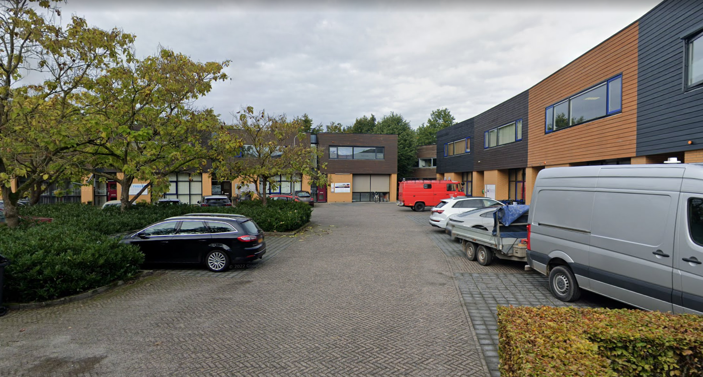 Een grijze, bewolkte dag bij een bedrijventerrein met auto's geparkeerd voor de gebouwen.