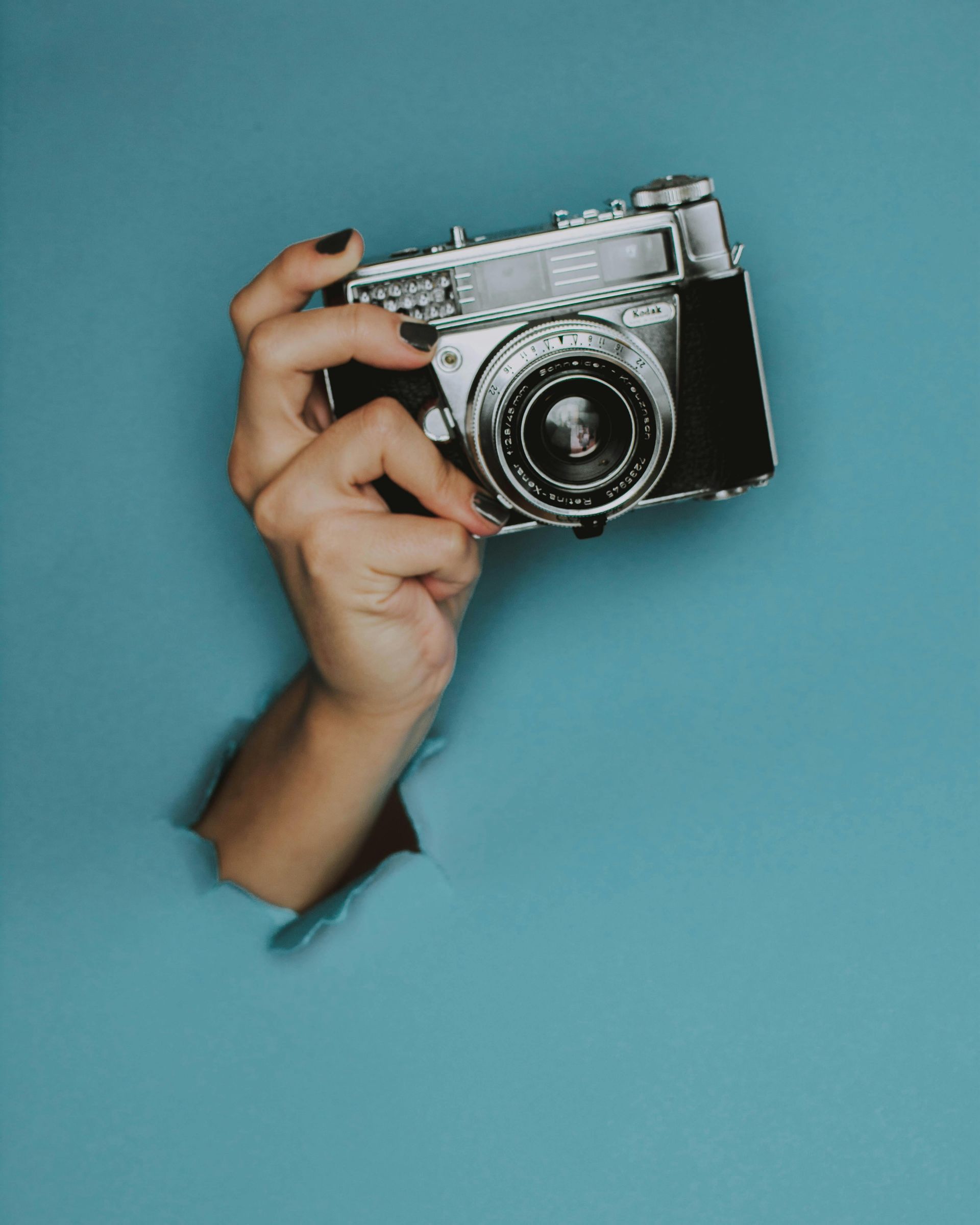 Hand die een zilverkleurige vintage camera vasthoudt, komt tevoorschijn tegen een blauwe achtergrond.