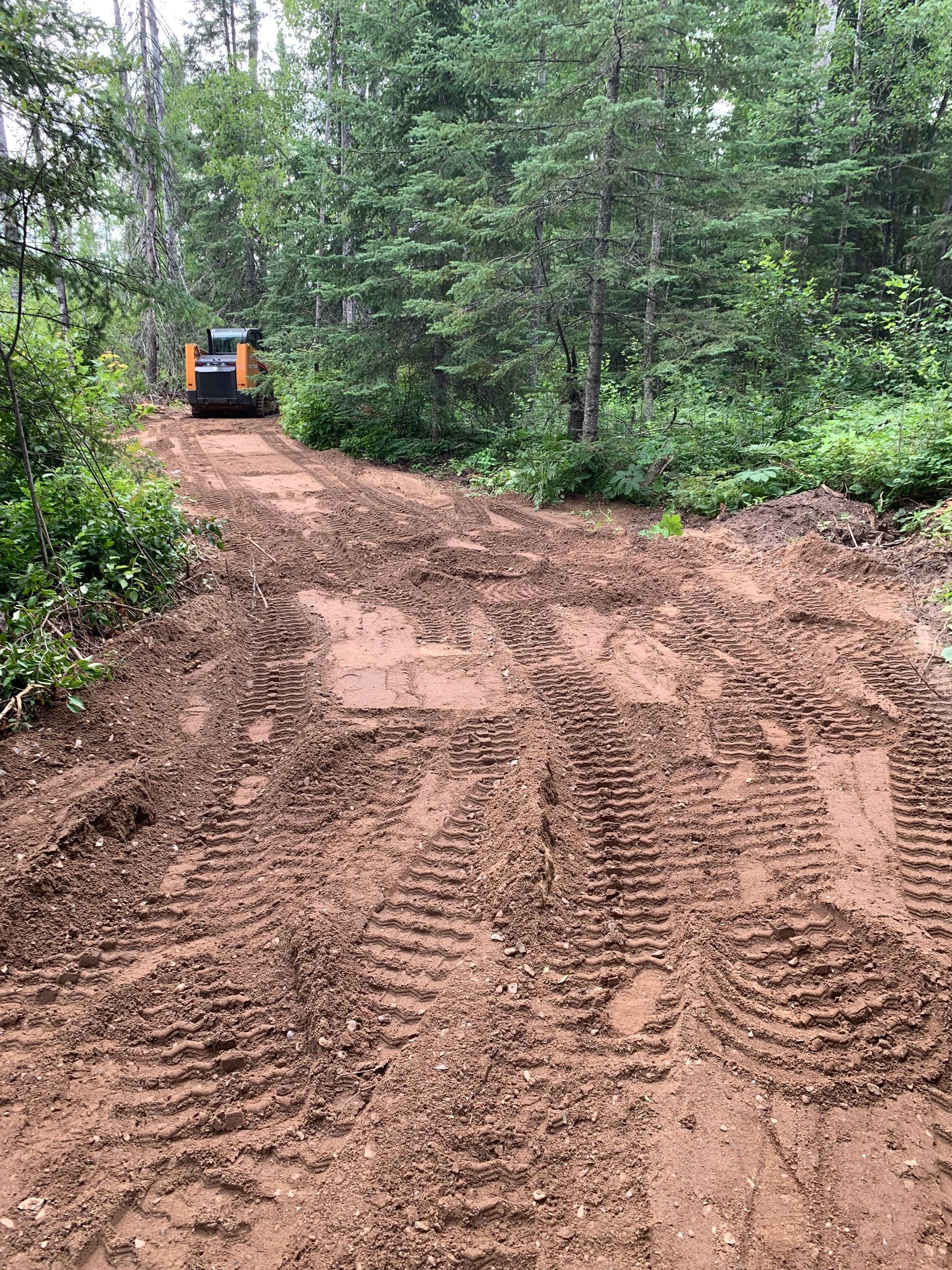 Mud-covered dirt road in a forest, with a small construction vehicle in the distance.