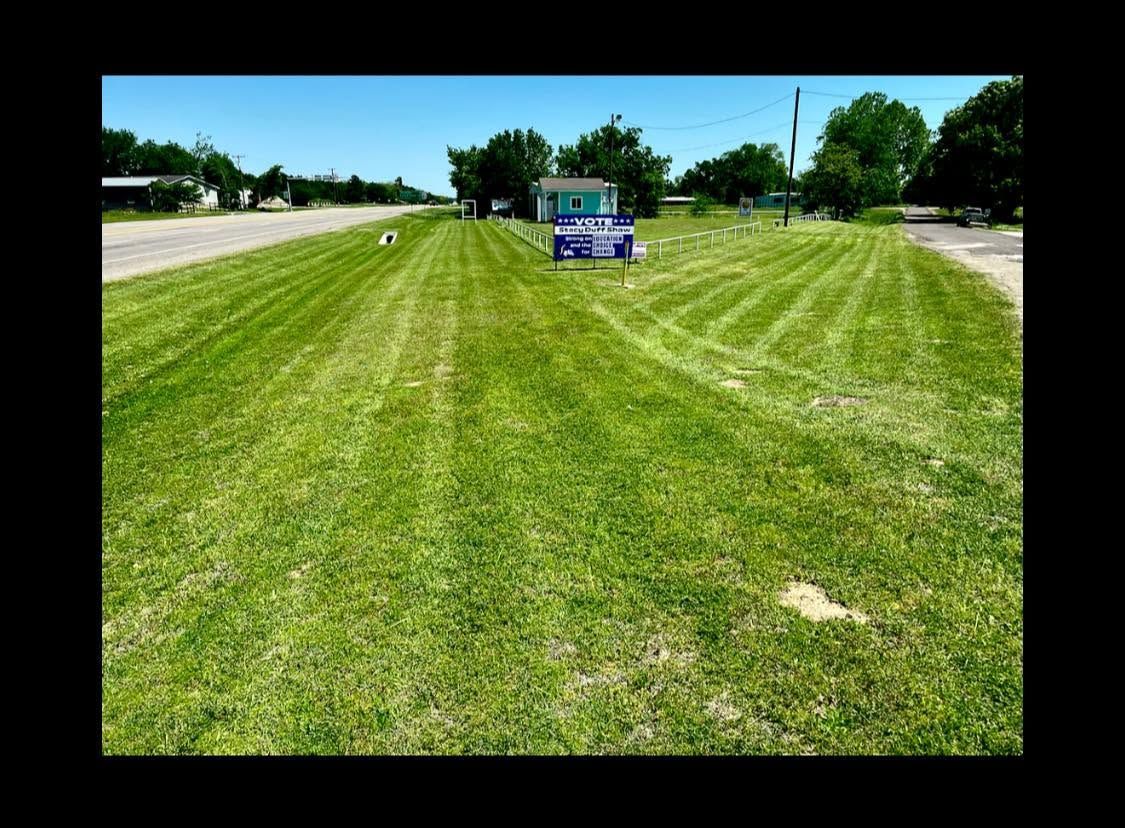 Wide mowed grassy field with a small tractor in the distance under a sunny sky