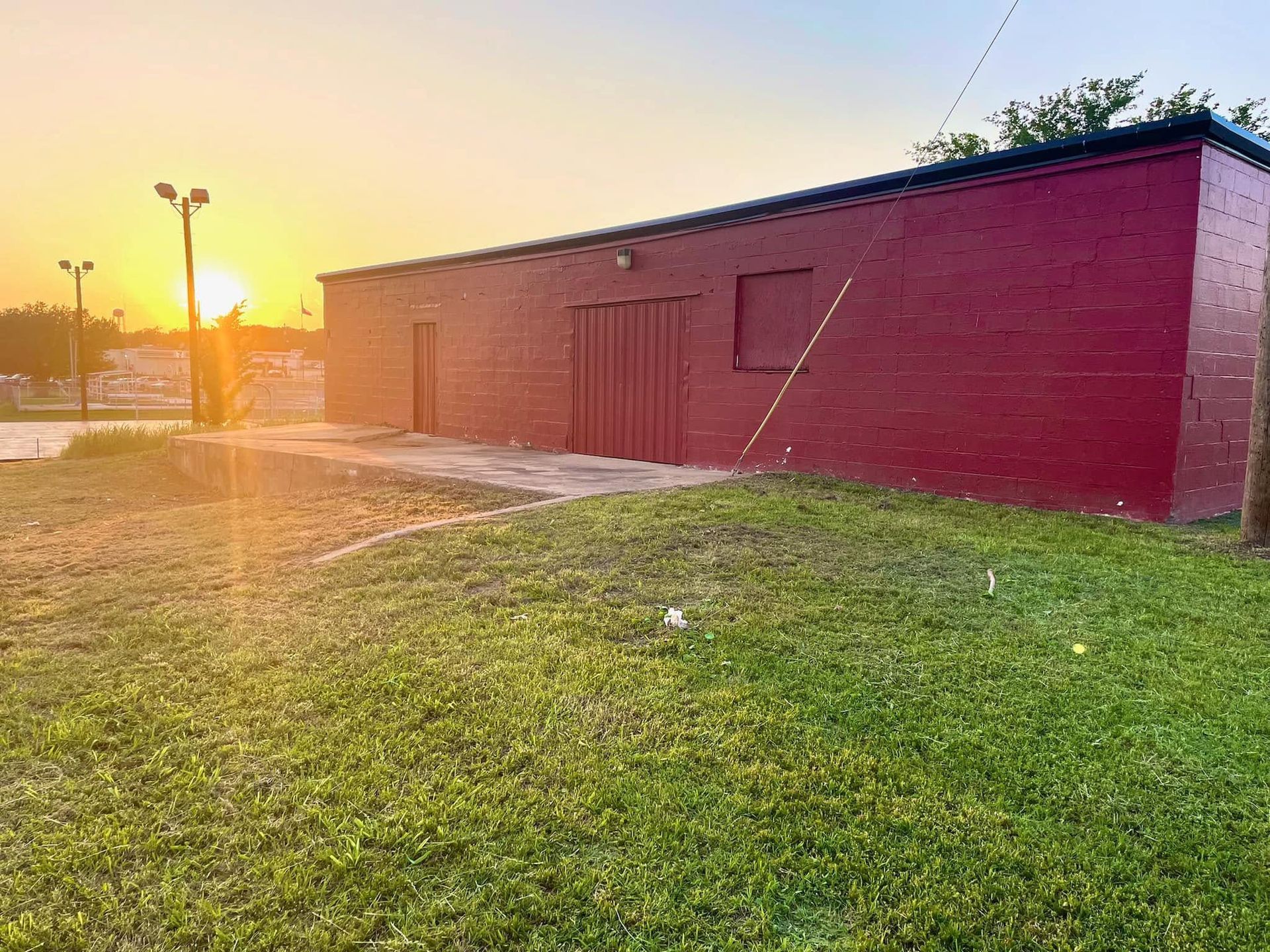 Red brick building at sunset beside a grassy field and lamp posts