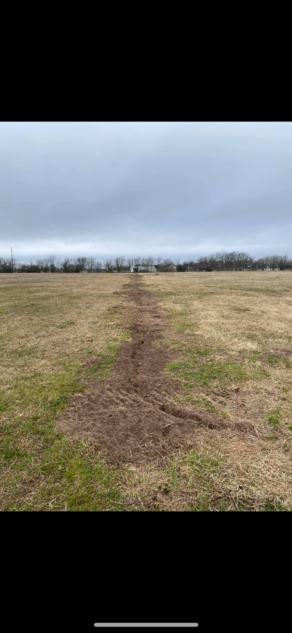 A muddy path cuts through a grassy field under a cloudy gray sky.