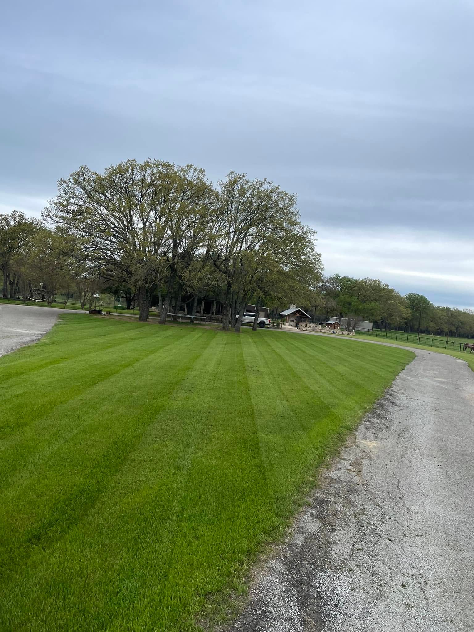 Gravel path beside a green lawn and trees under an overcast sky