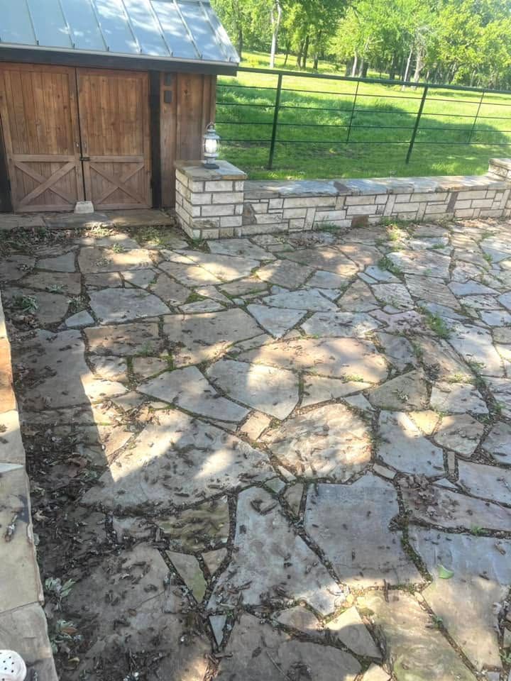 Stone patio beside a wooden shed and low stone wall in a sunny yard