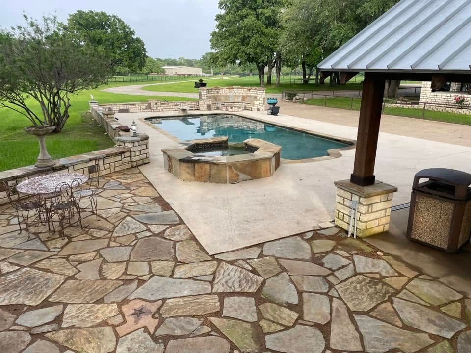 Stone patio with a built-in pool and fire pit overlooking a green golf course, under a covered pavilion