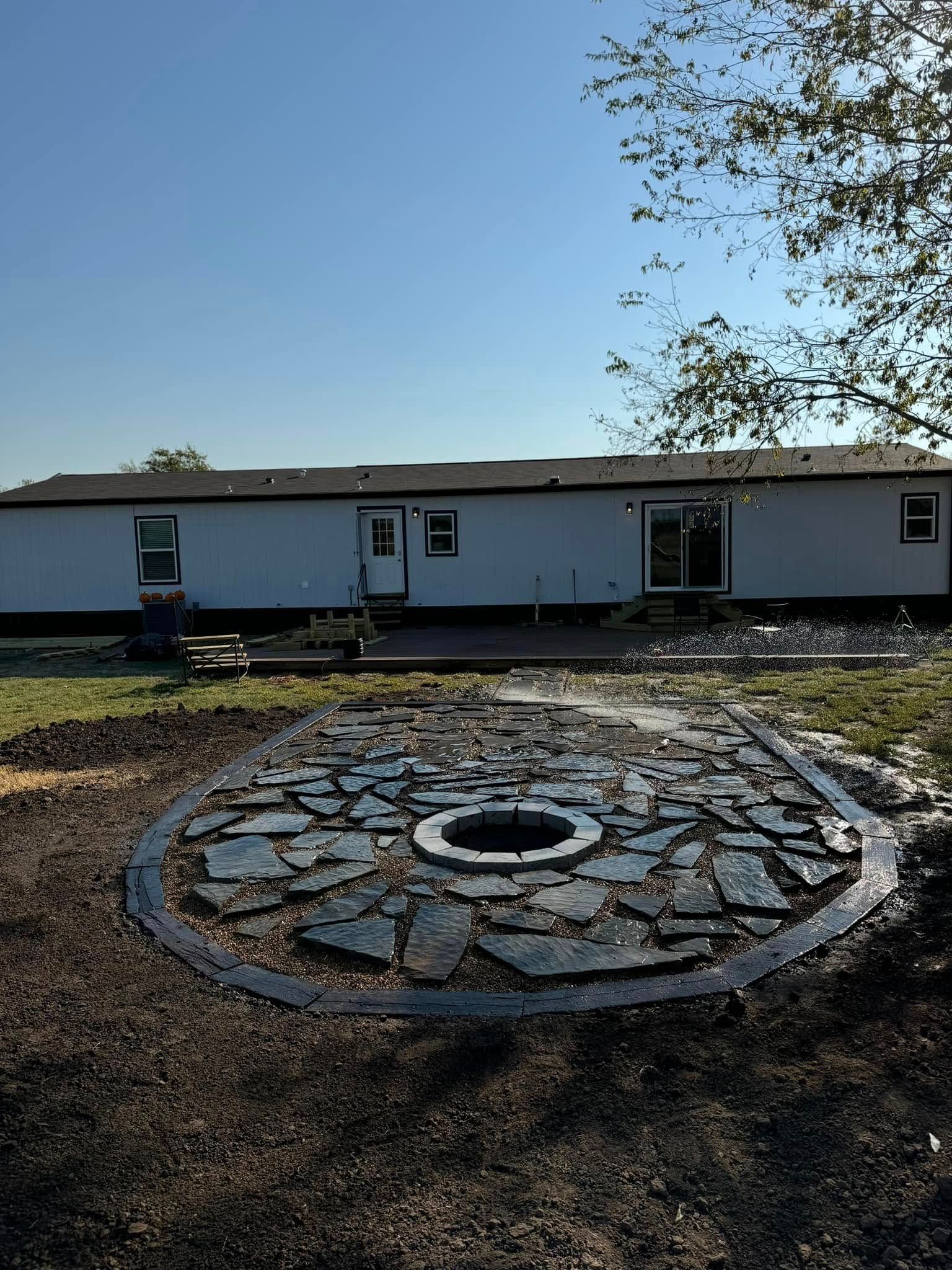 A rural house with a stone fire pit in the foreground under a clear blue sky.
