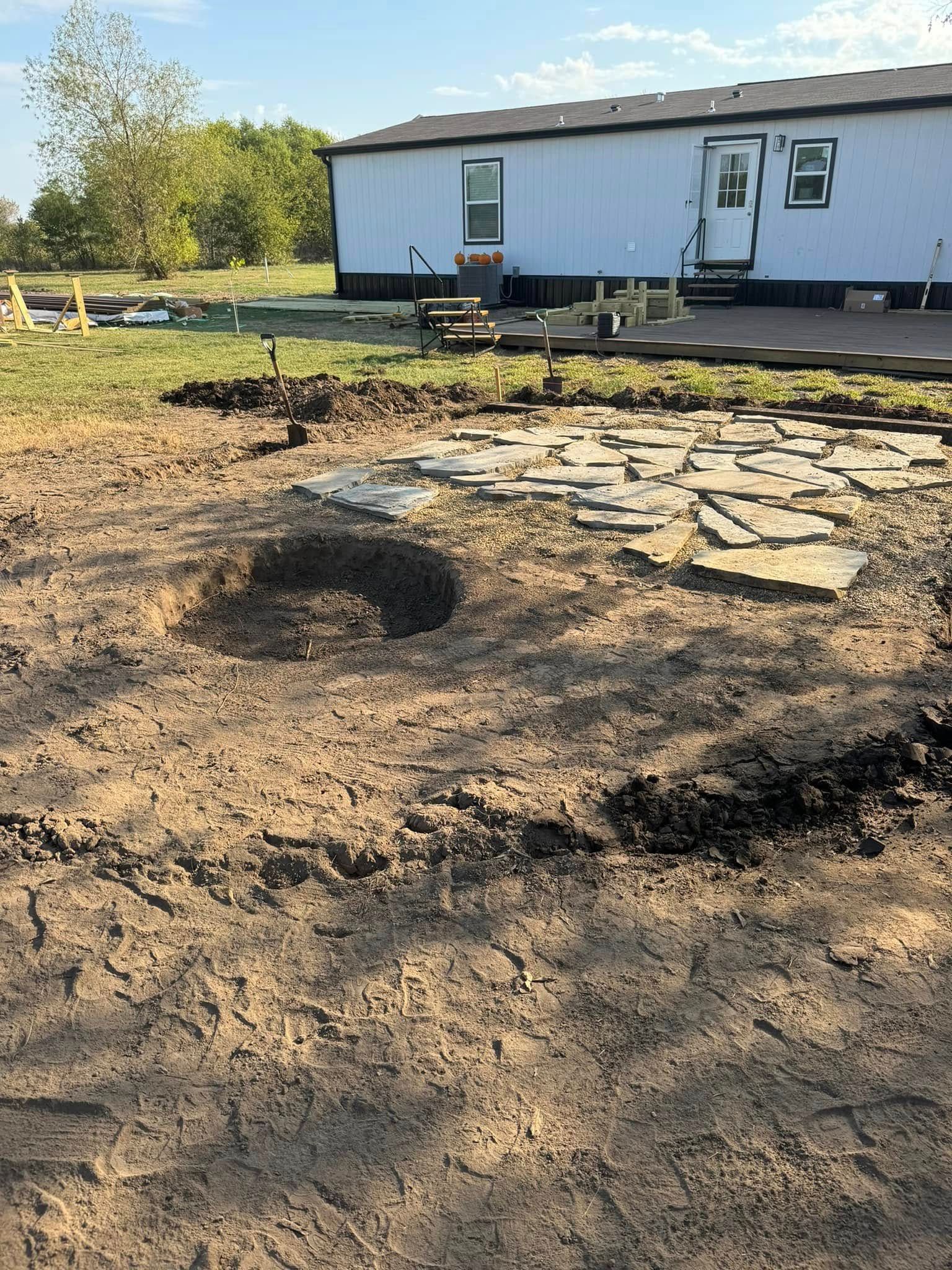 A muddy yard with a circular fire pit and a white mobile home in the background.