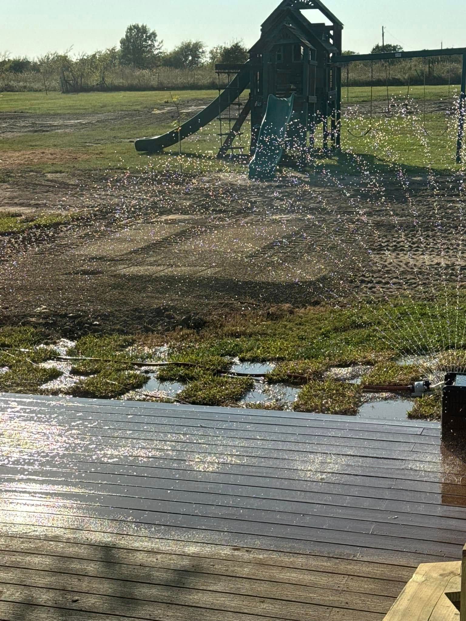 Irrigation sprinkler spraying water across a grassy field near a puddled path at sunset