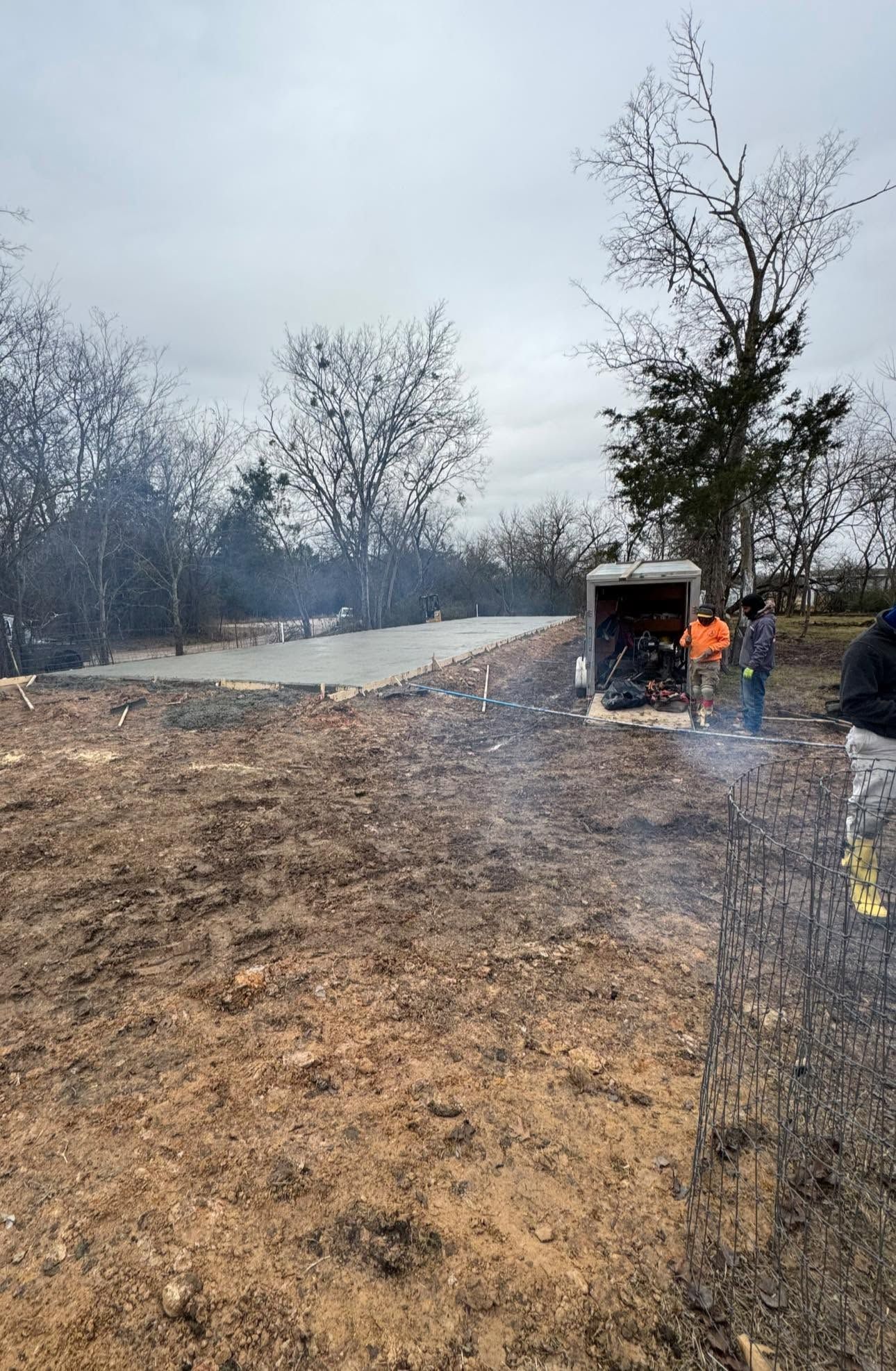 Burned field with charred trees and a person in an orange jacket near a small structure