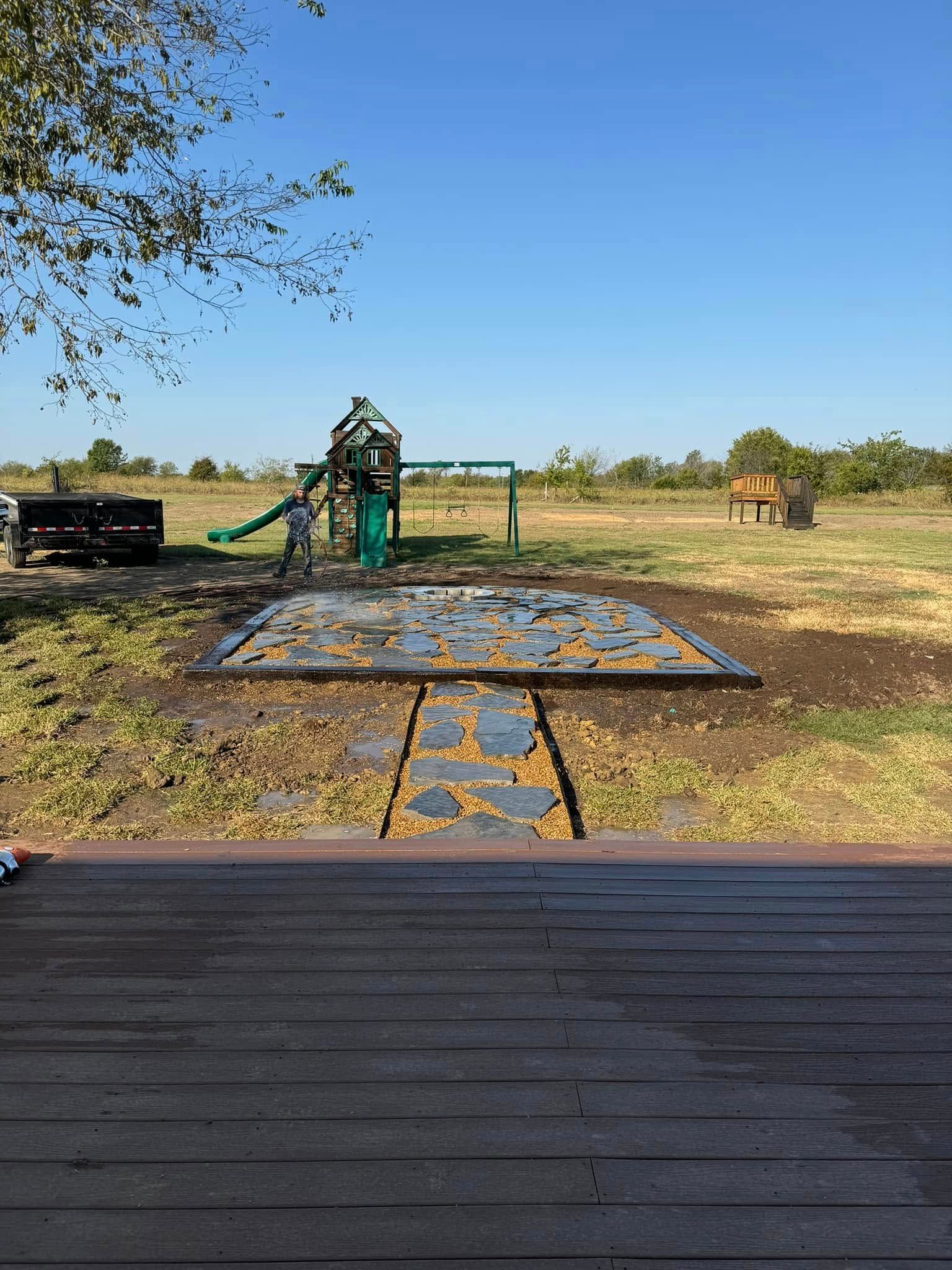 Playground with blue safety mat, swings, and slide in a dry, open park under clear sky