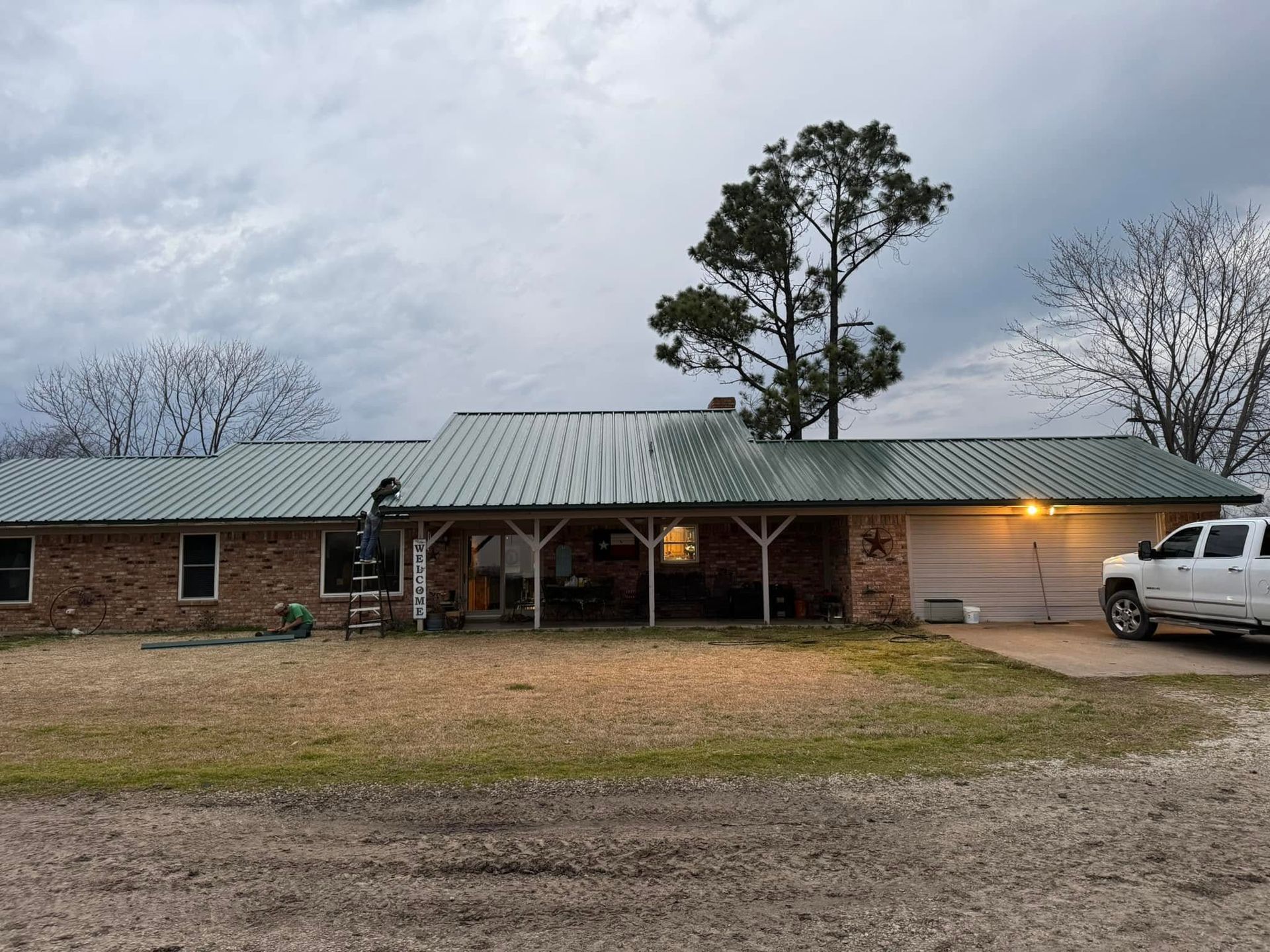 Single-story brick building with metal roof at dusk, lit porch, parked white van, and bare trees.