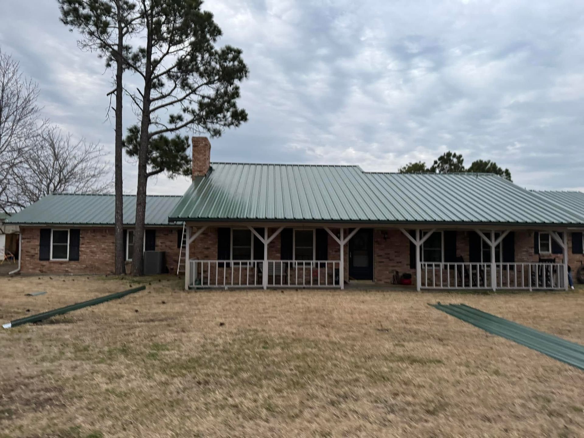 Single-story brick house with green metal roof and front porch on a cloudy day