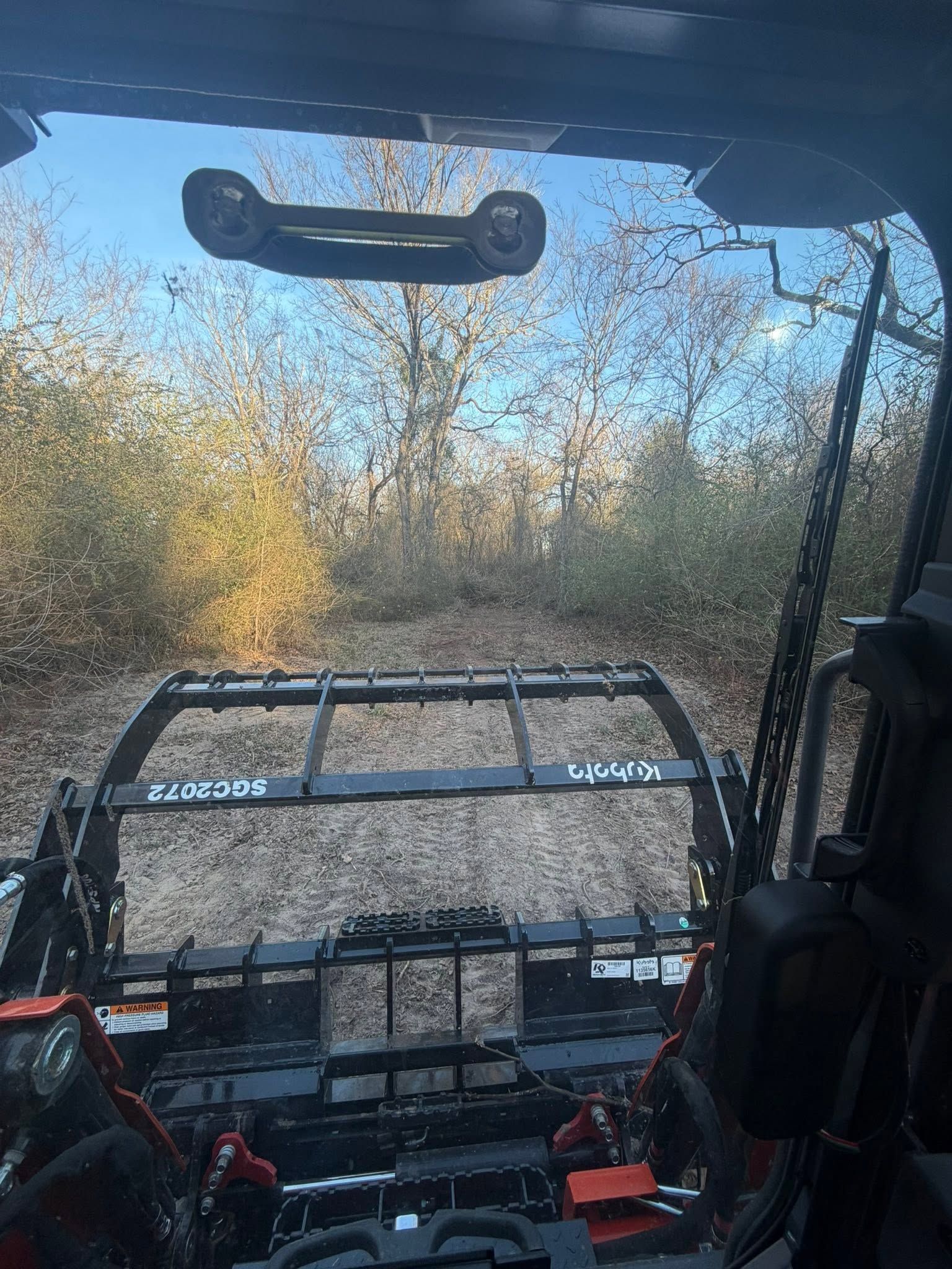 Off-road vehicle cabin facing a gravel trail through autumn brush, with a front cargo rack visible ahead