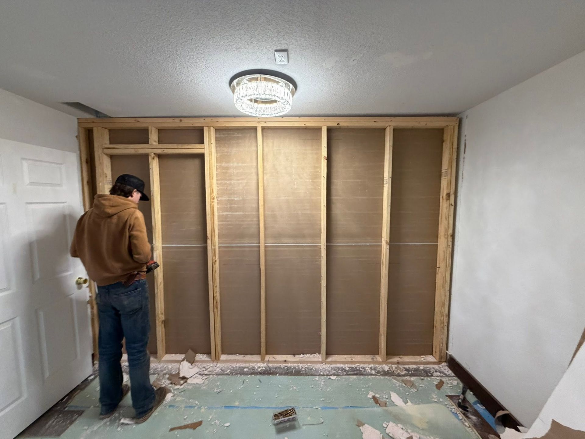 Person working in a room with wall studs exposed and debris on the floor during renovation.