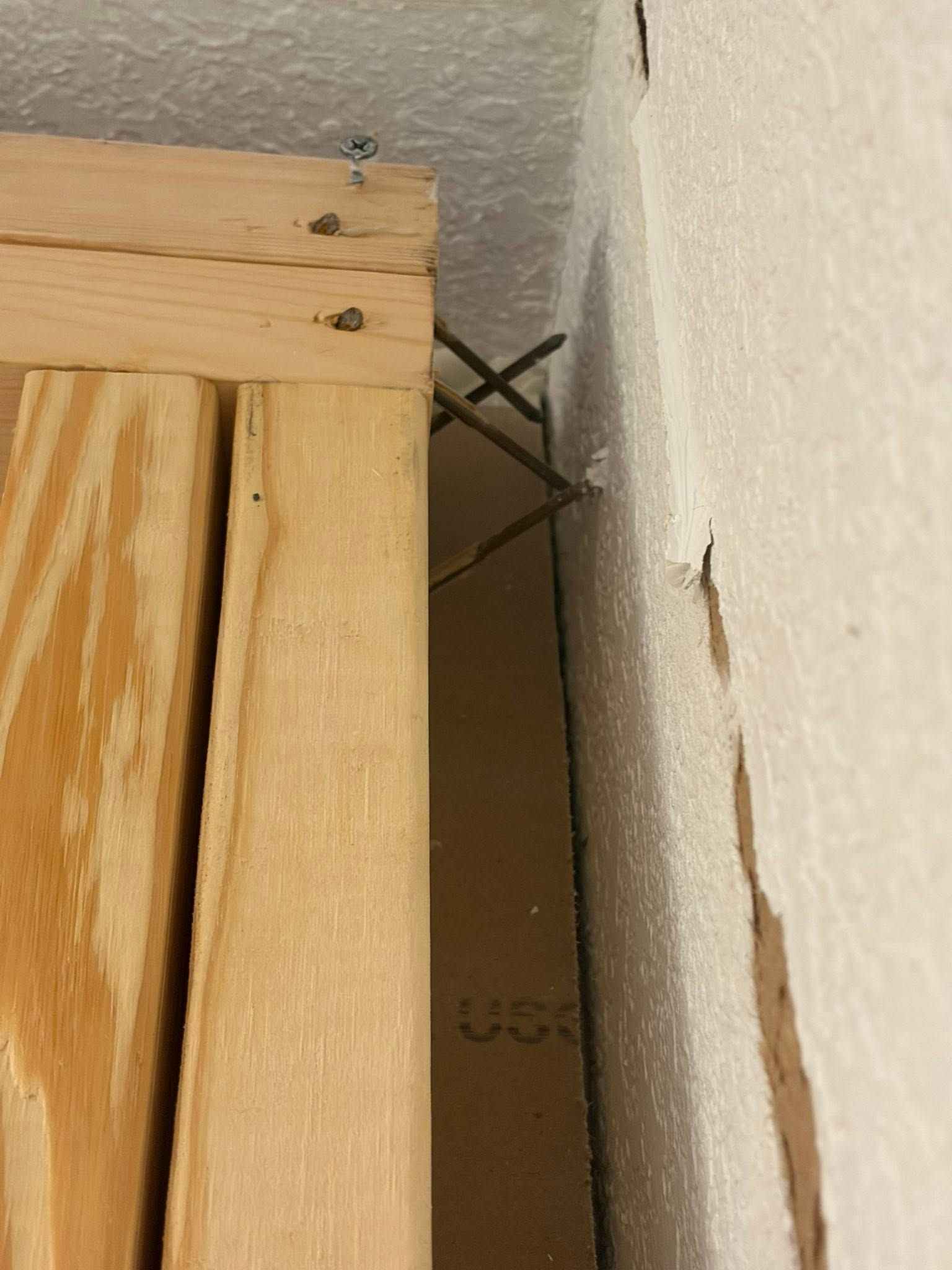 Close-up of a wooden frame beside a white wall, showing a narrow gap and a metal brace behind it