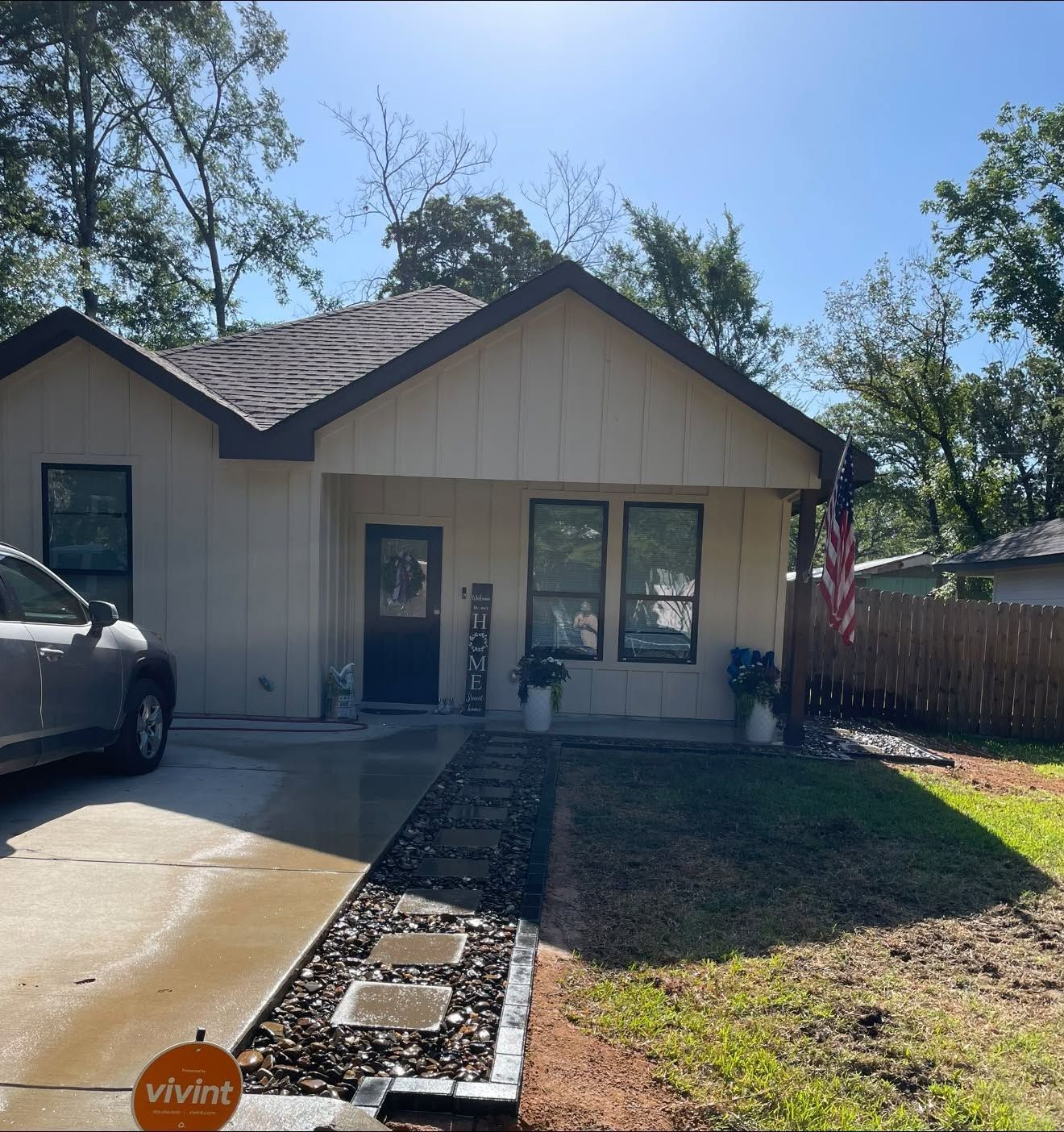 Small beige house with dark roof, front walkway, driveway, and a parked car on a sunny day
