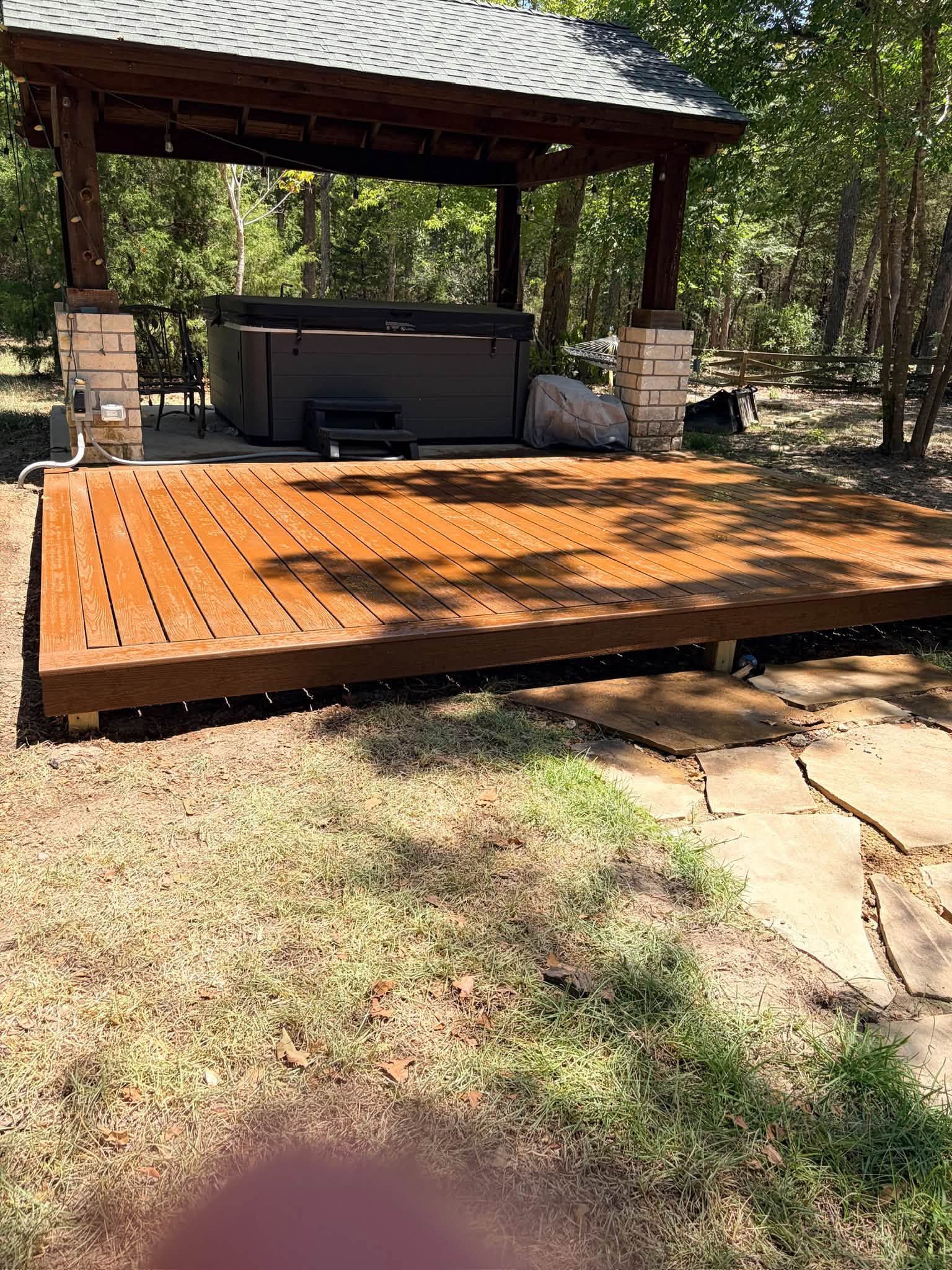 Wooden deck with a covered hot tub surrounded by trees and dirt ground