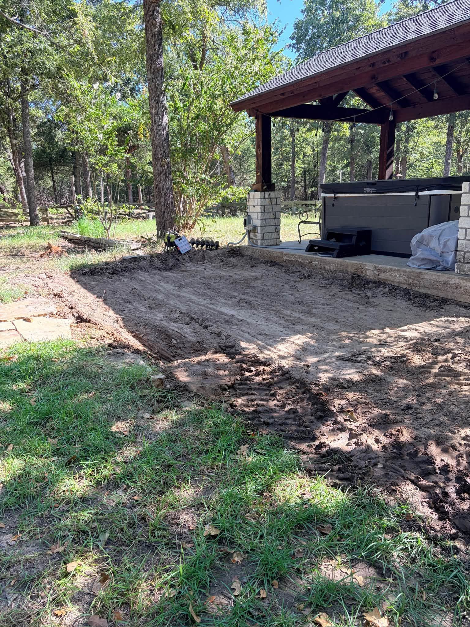 Freshly tilled garden bed beside a covered patio in a wooded backyard