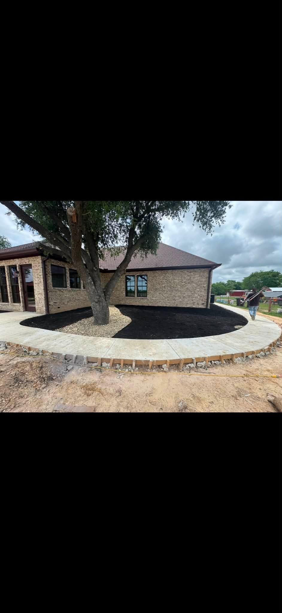 Stone house with a dark roof and circular gravel driveway, framed by trees under a cloudy sky