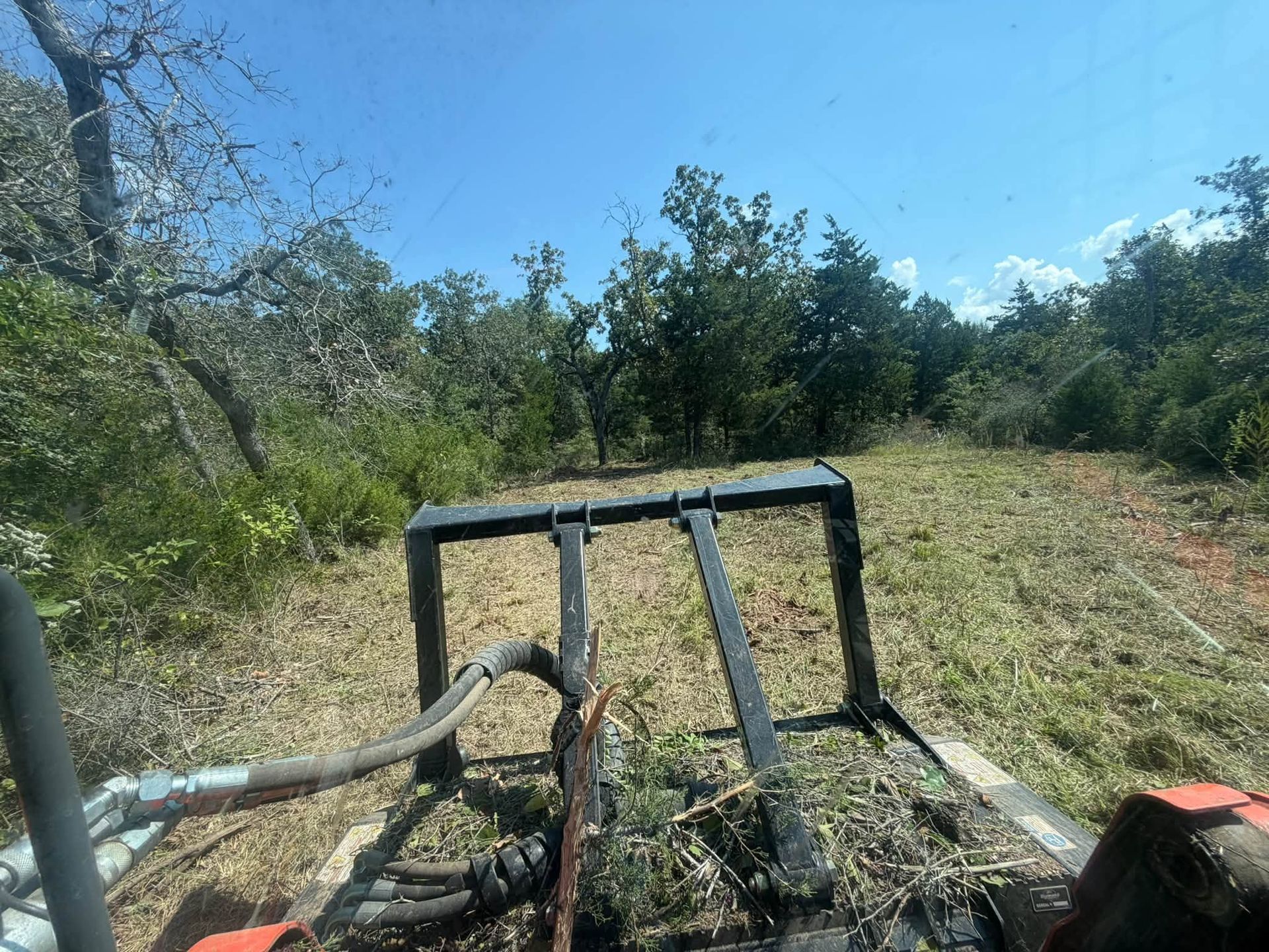 Farm tractor towing brush through a sunny grassy field with trees in the background