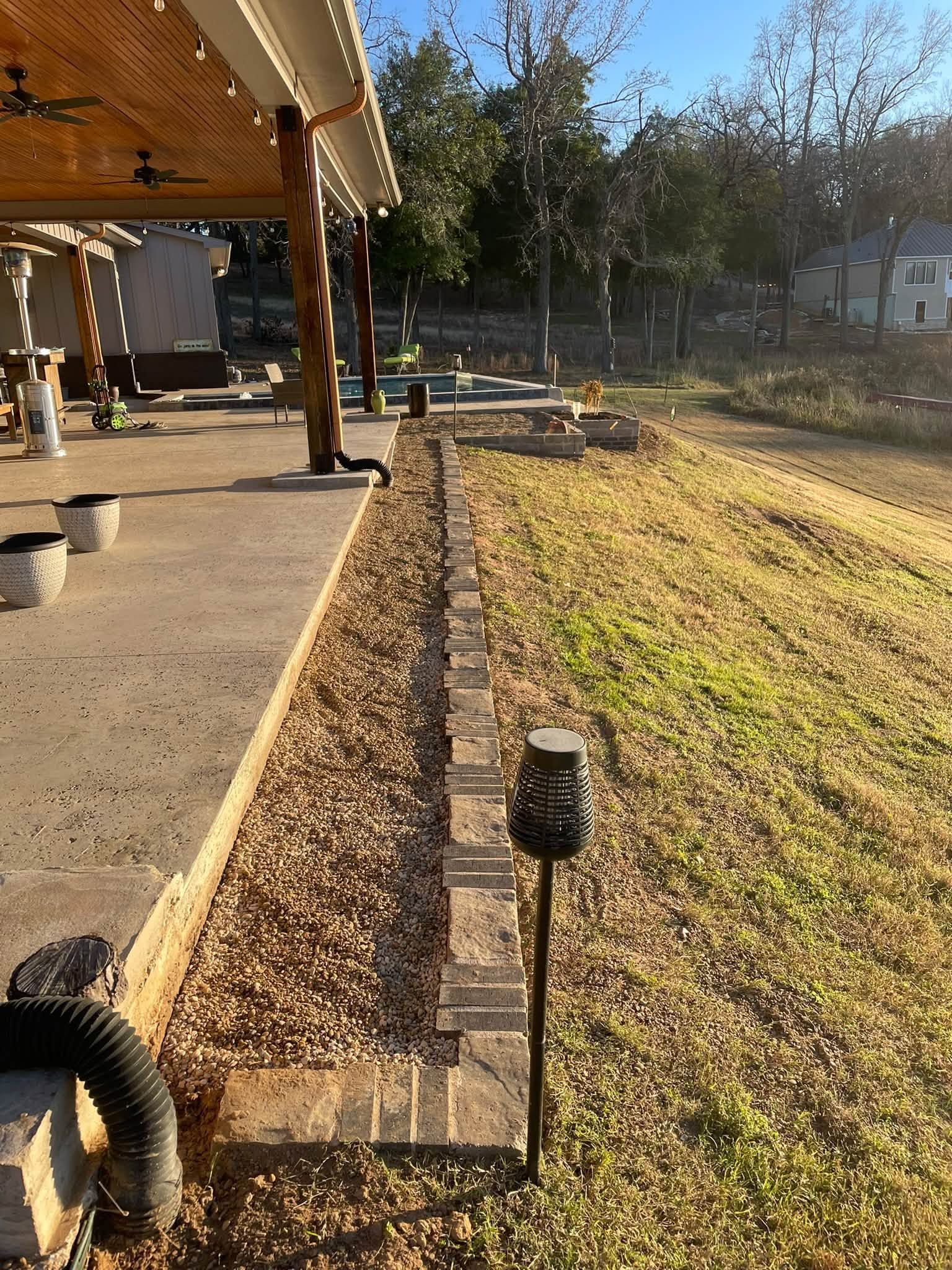 Backyard with covered patio, gravel border, lawn, and a small landscape light in the foreground