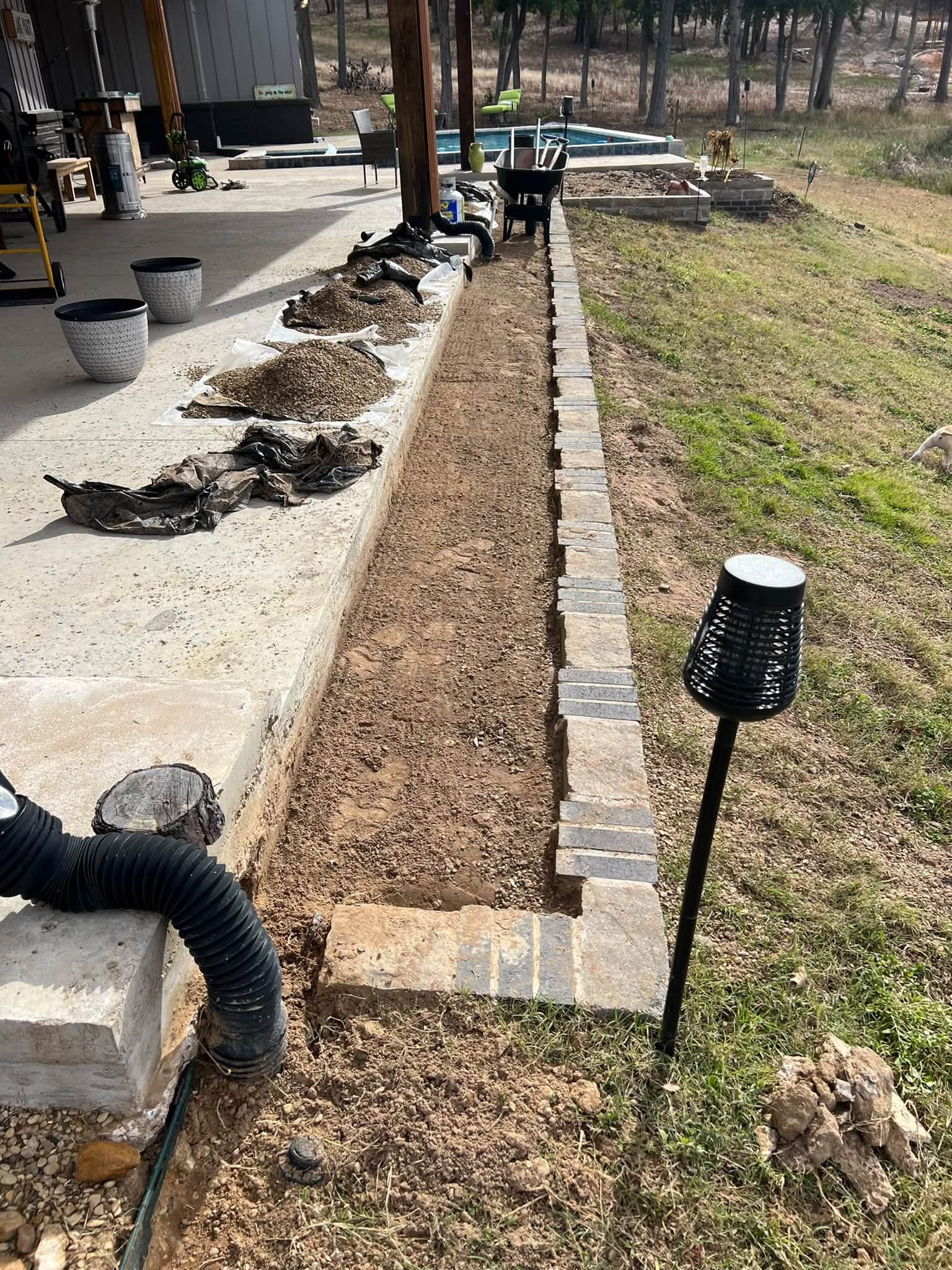 Landscaped garden bed beside a concrete path, with black solar lights and scattered mulch under construction.