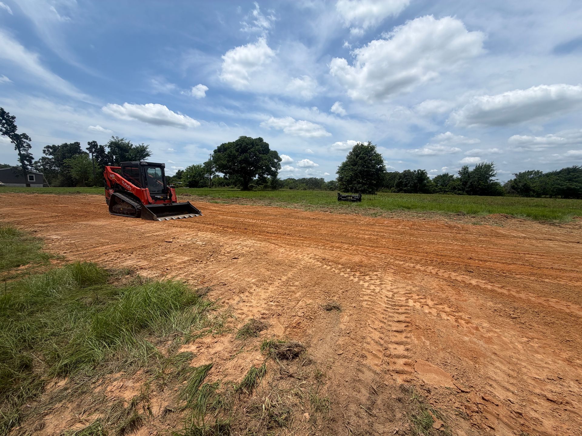 Red tractor grading a dirt field under a cloudy sky