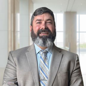 Man in gray suit and tie smiles in office setting.
