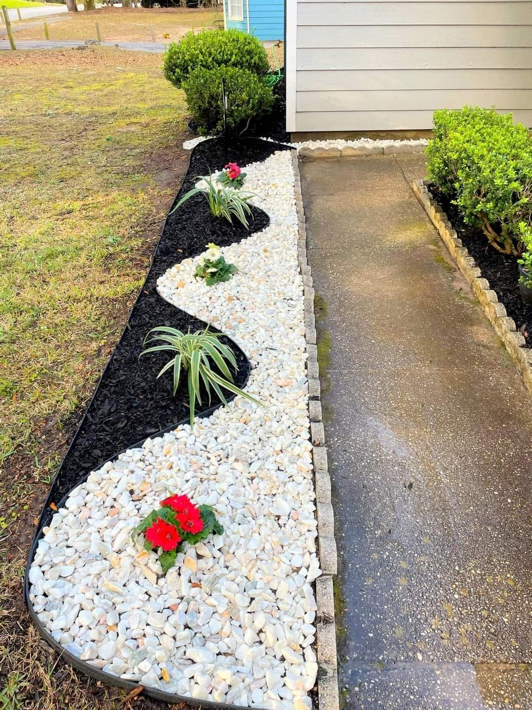 A garden filled with white rocks and red flowers next to a sidewalk.