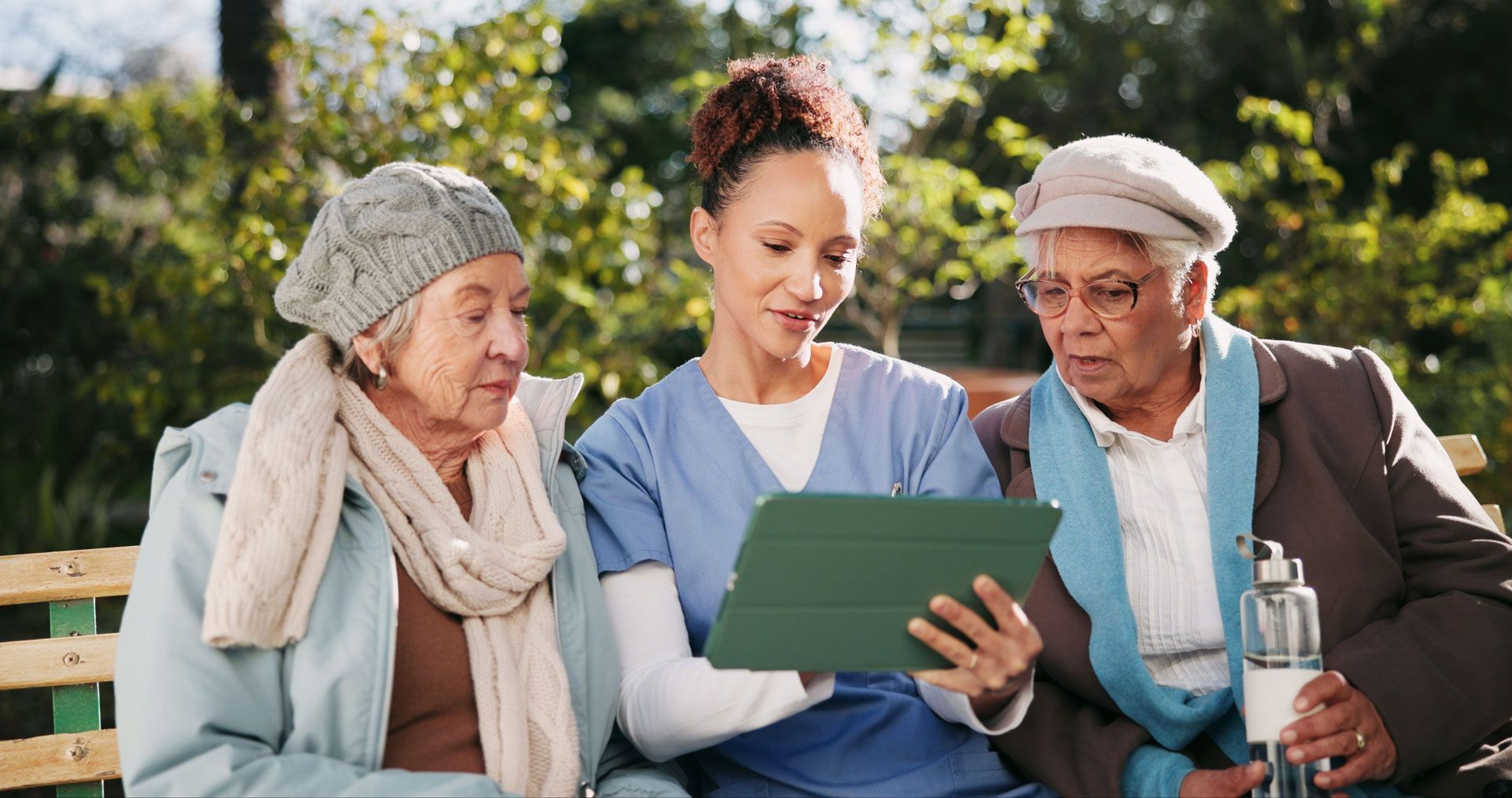 Caregiver shows tablet to two seniors seated outside.