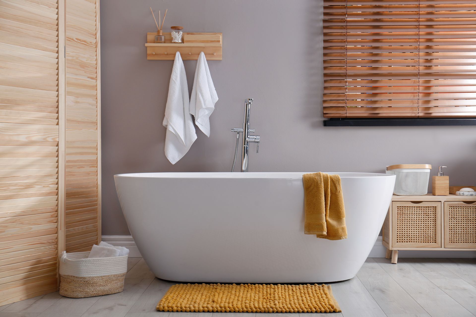 Modern bathroom with a white bathtub, yellow accents, and wooden blinds.
