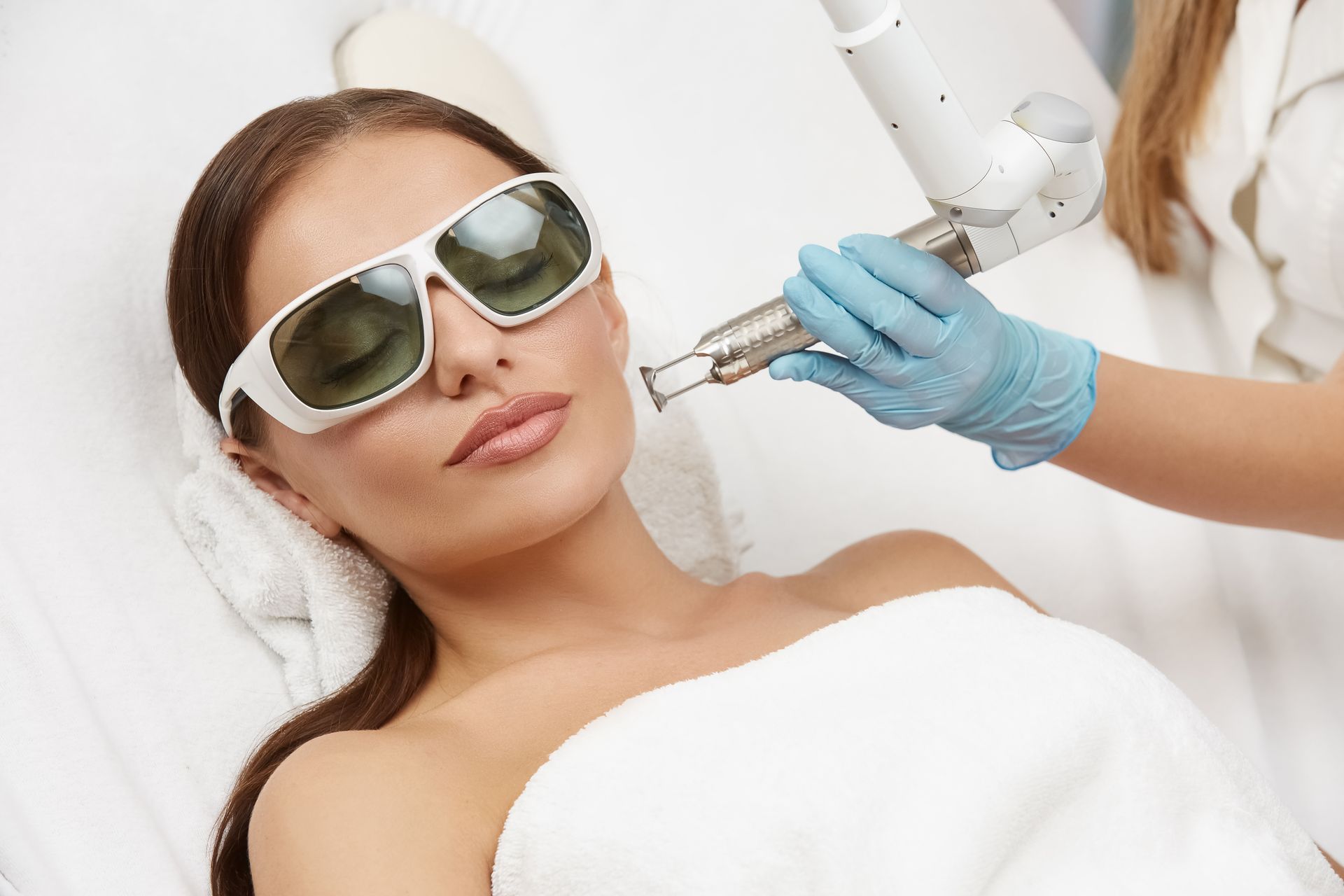 Woman wearing sunglasses receives a cosmetic facial treatment with a handheld device in a clinic