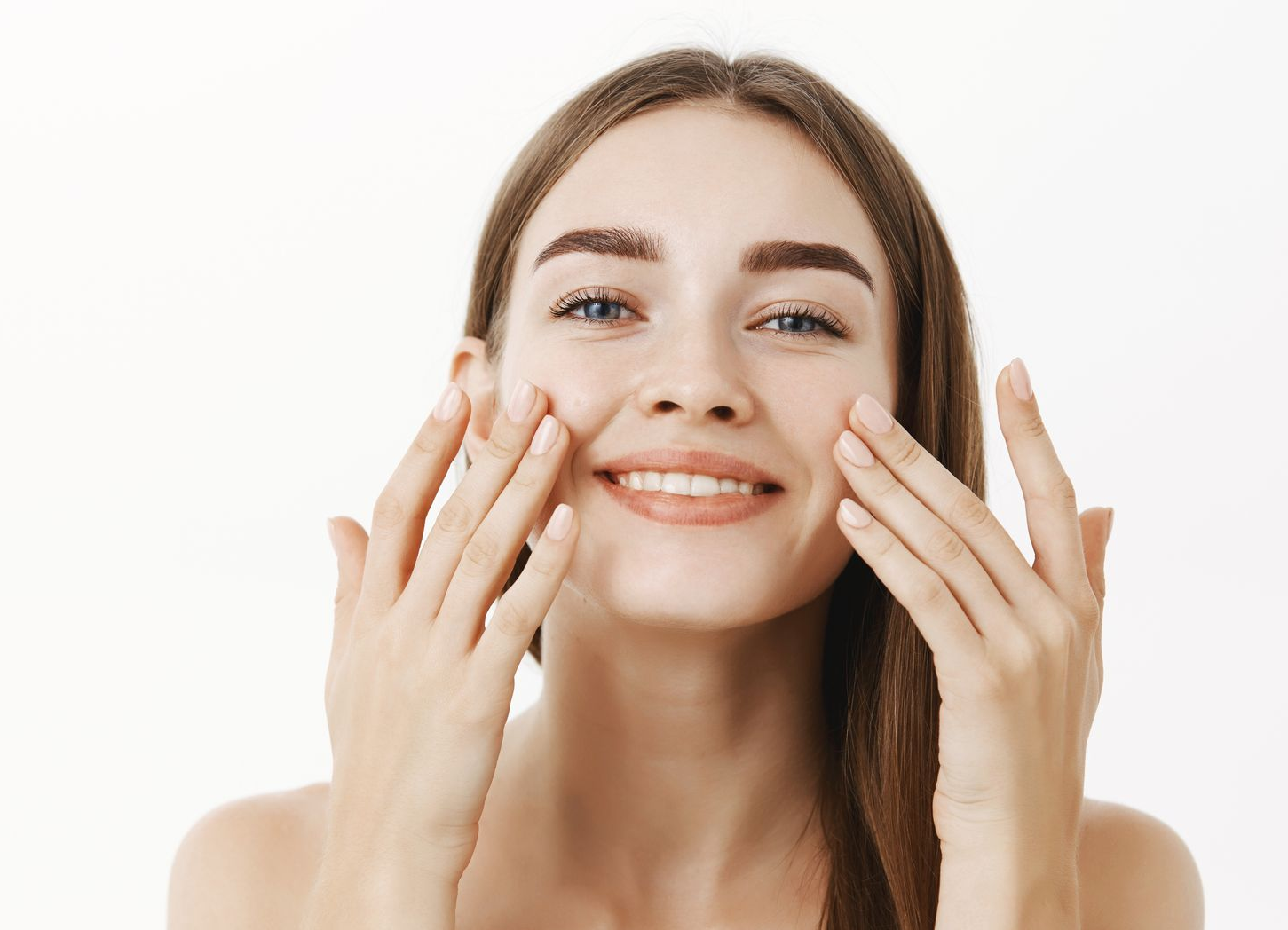 Smiling woman applying skincare cream to her cheeks against a white background